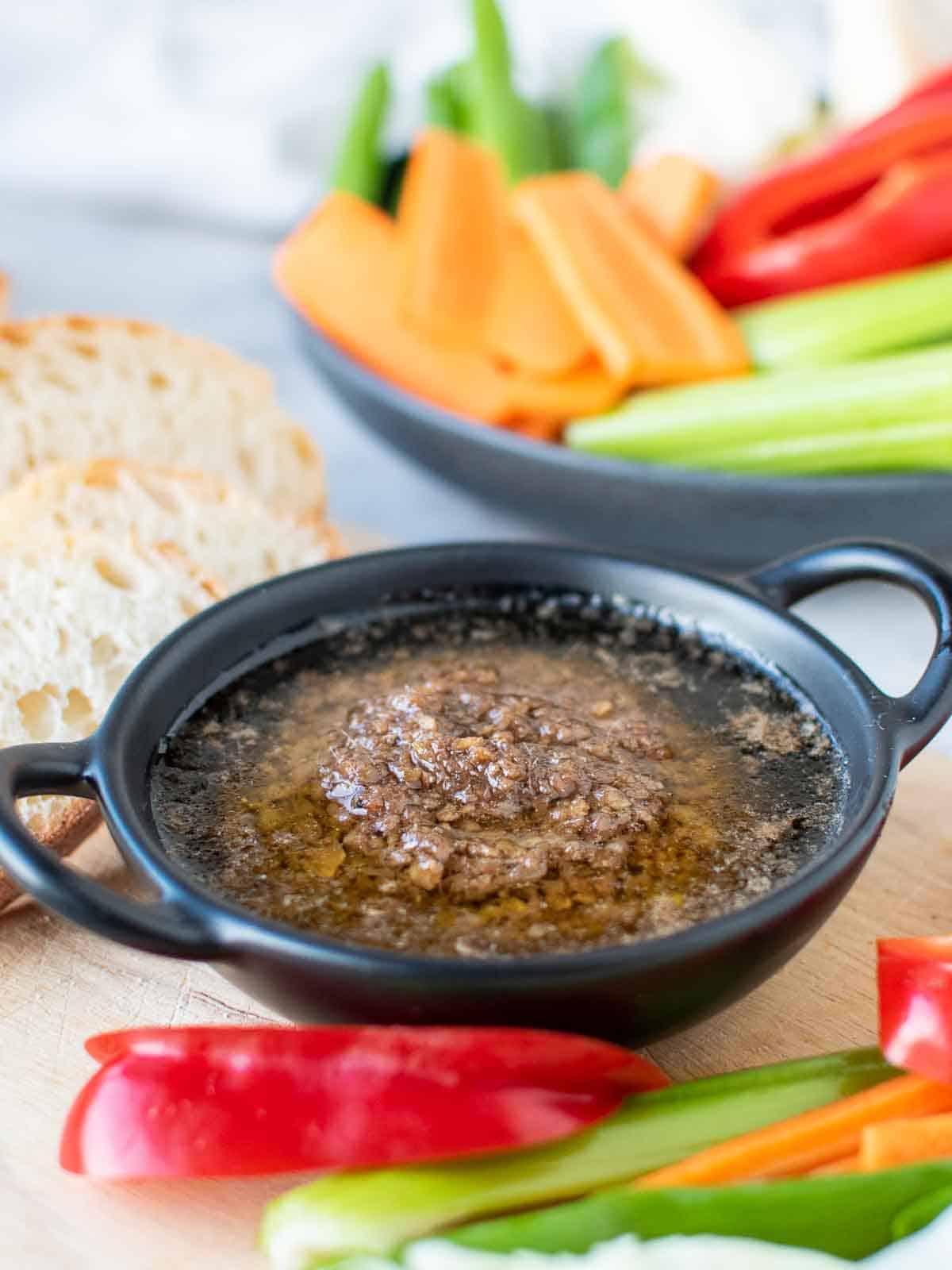 Bagna cauda sauce in a black dish surrounded by sliced vegetables and bread.