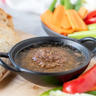 Bagna cauda sauce in a black dish surrounded by sliced vegetables and bread