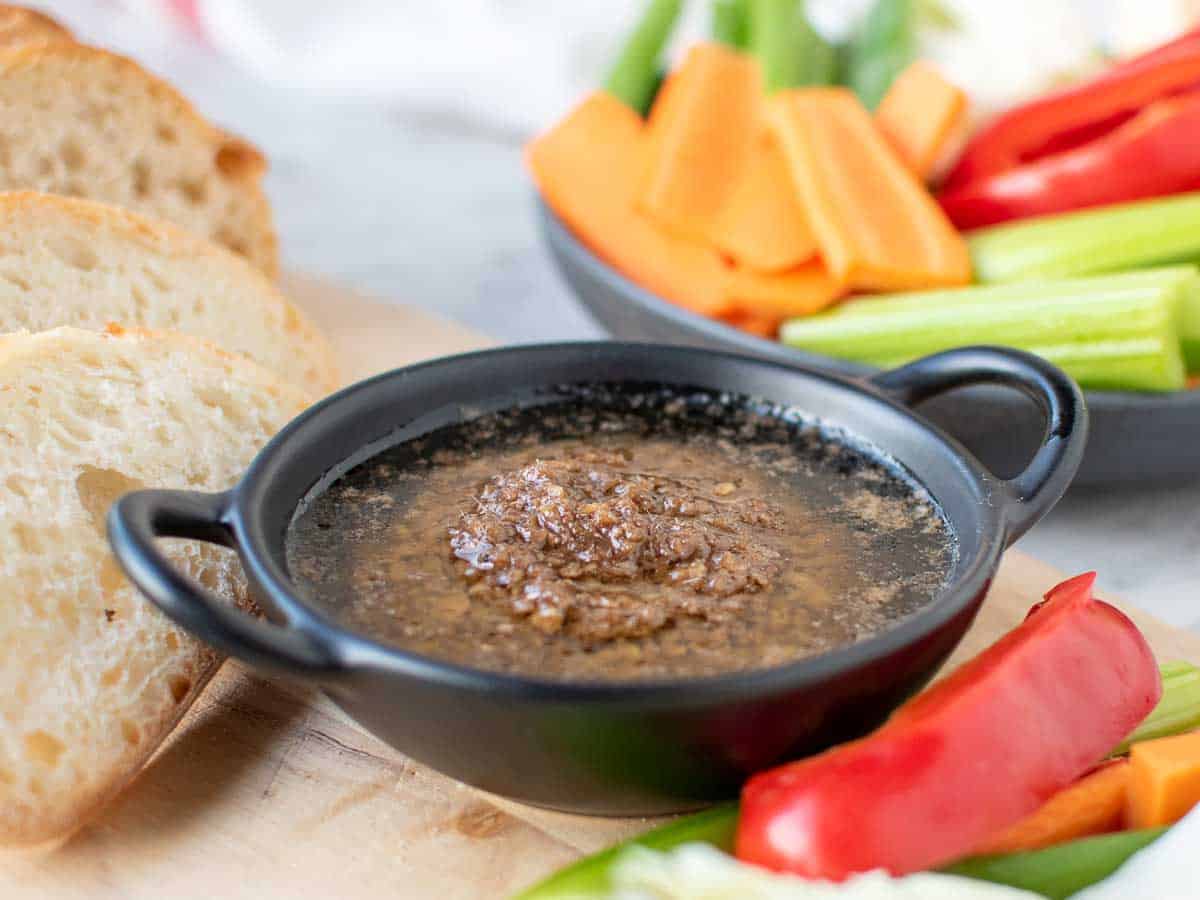 hot dipping sauce in a black dish surrounded by sliced vegetables and bread.