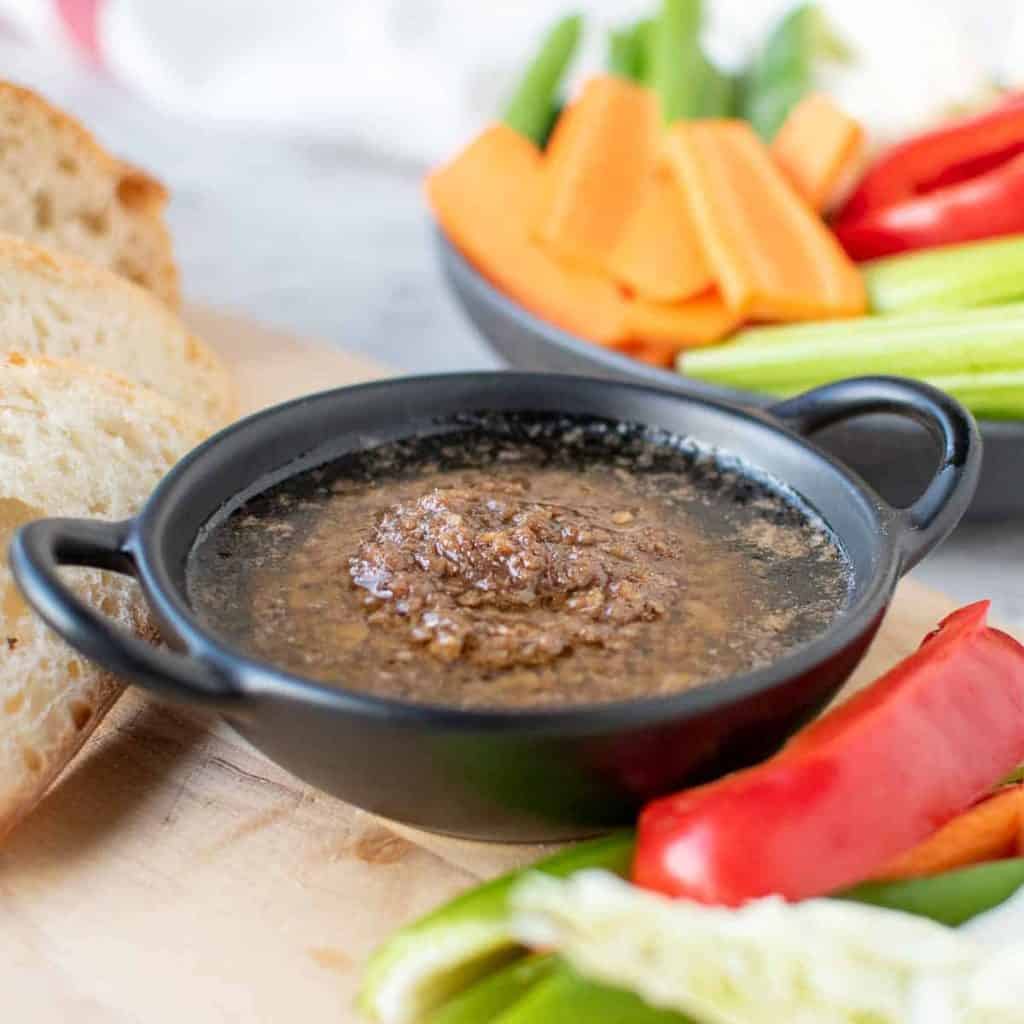 Bagna cauda sauce in a black dish surrounded by sliced vegetables and bread