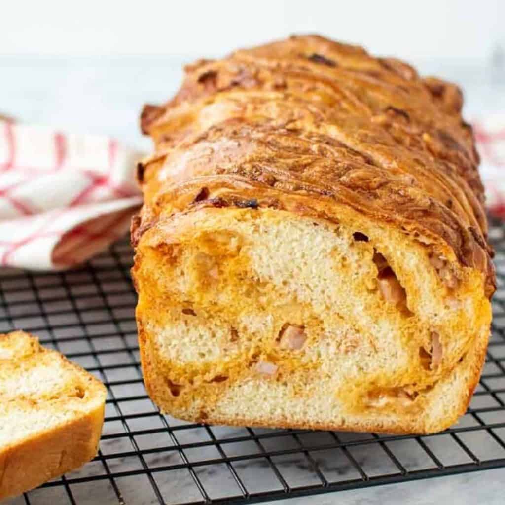 Cross section of cheese filled Bread loaf on black wire rack with a slice of bread on the side and red and white cloth in the background