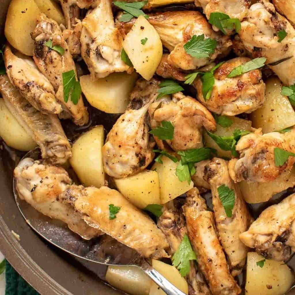 close up of braised chicken wings with potato chunks sprinkled with chopped parsley viewed from above