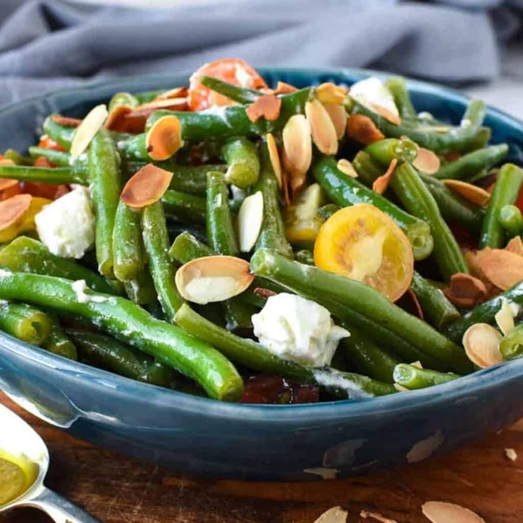 green bean salad with tomatoes and feta in blue bowl on wooden board