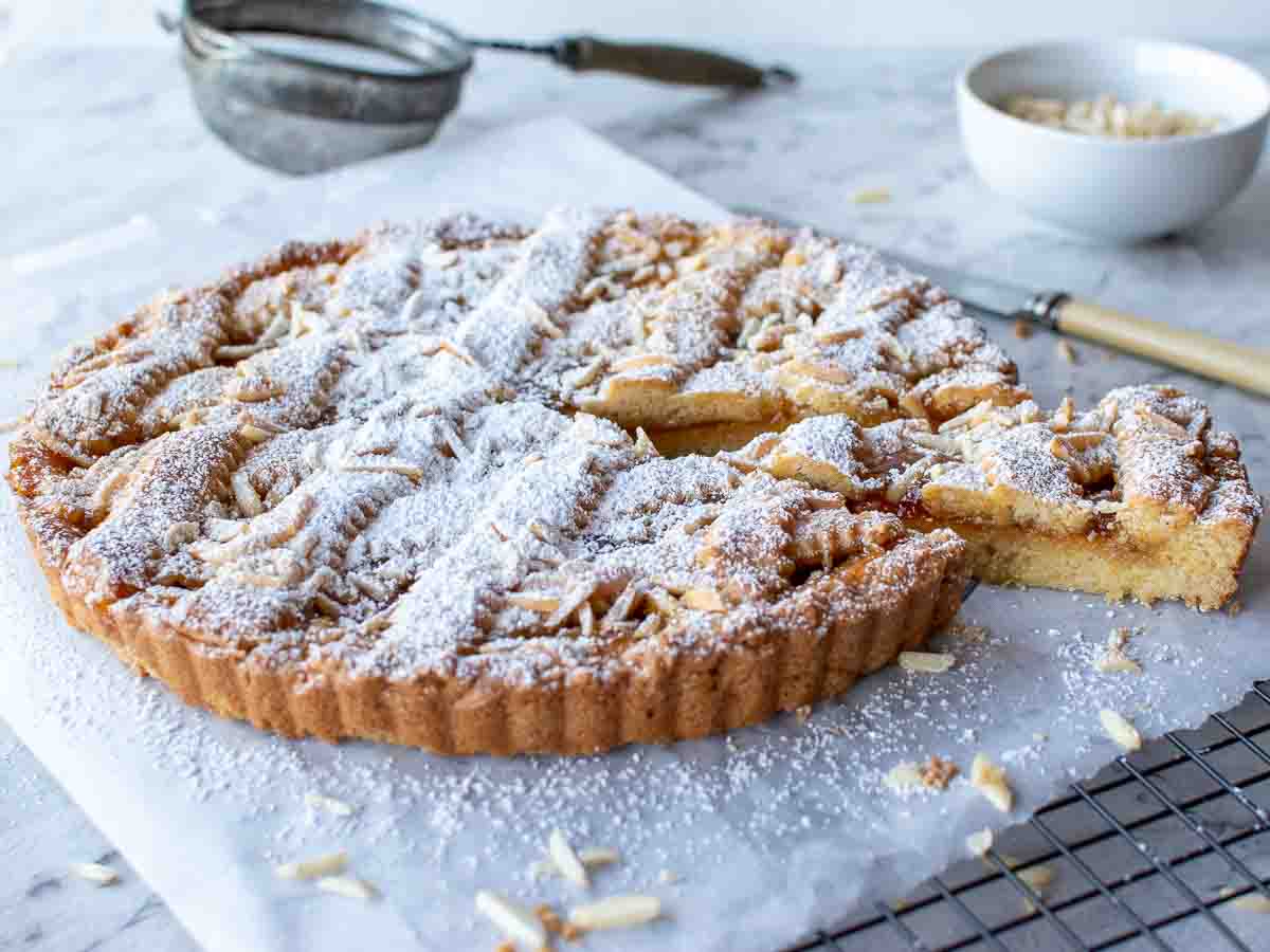 jam tart with lattice top sprinkled with powdered sugar with a slice cut.