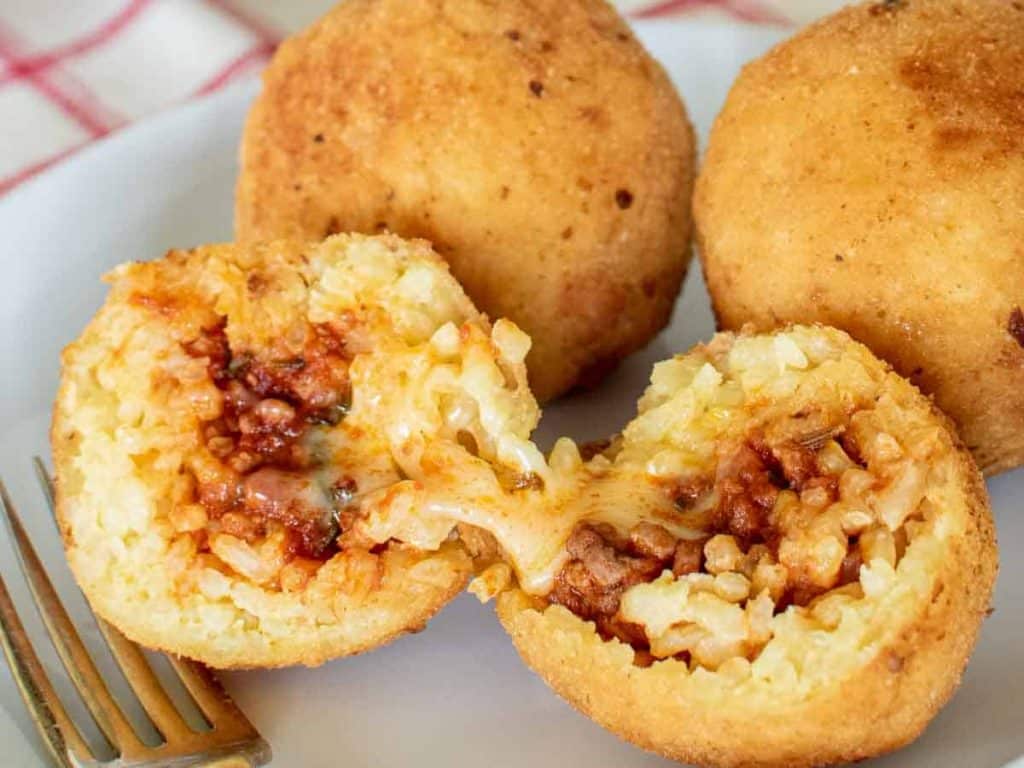 close up of inside an arancino with two arancini in the background