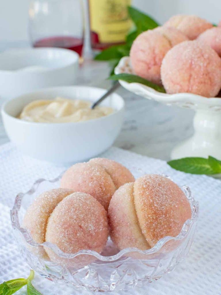 three Italian peach cookies in glass bowl with more cookies in the background