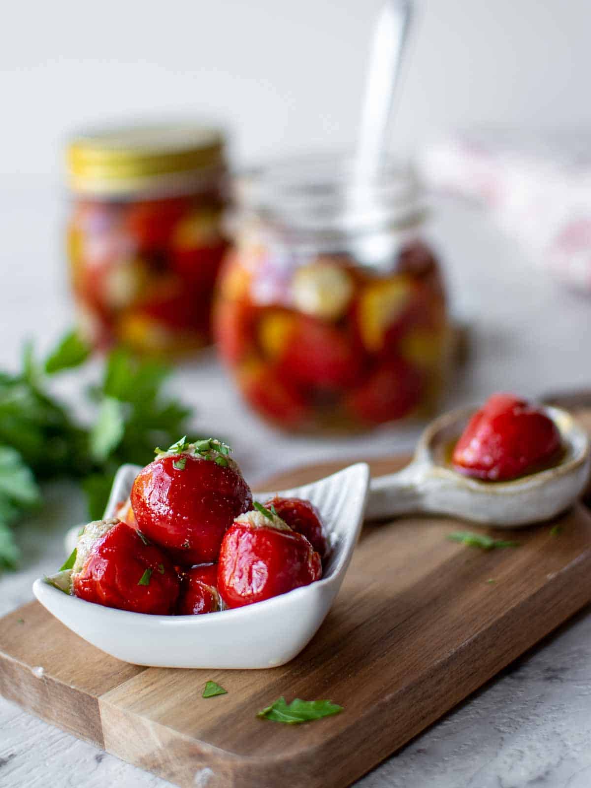 pile of stuffed cherry peppers in a white dish and one in a spoon with bottles filled in the background