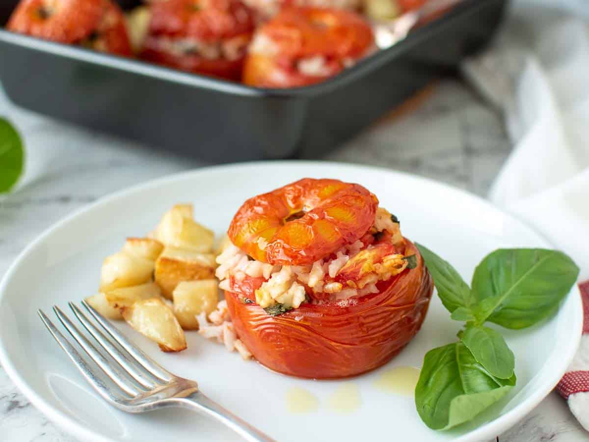 one baked tomato stuffed with rice on a white plate with cubed potatoes.