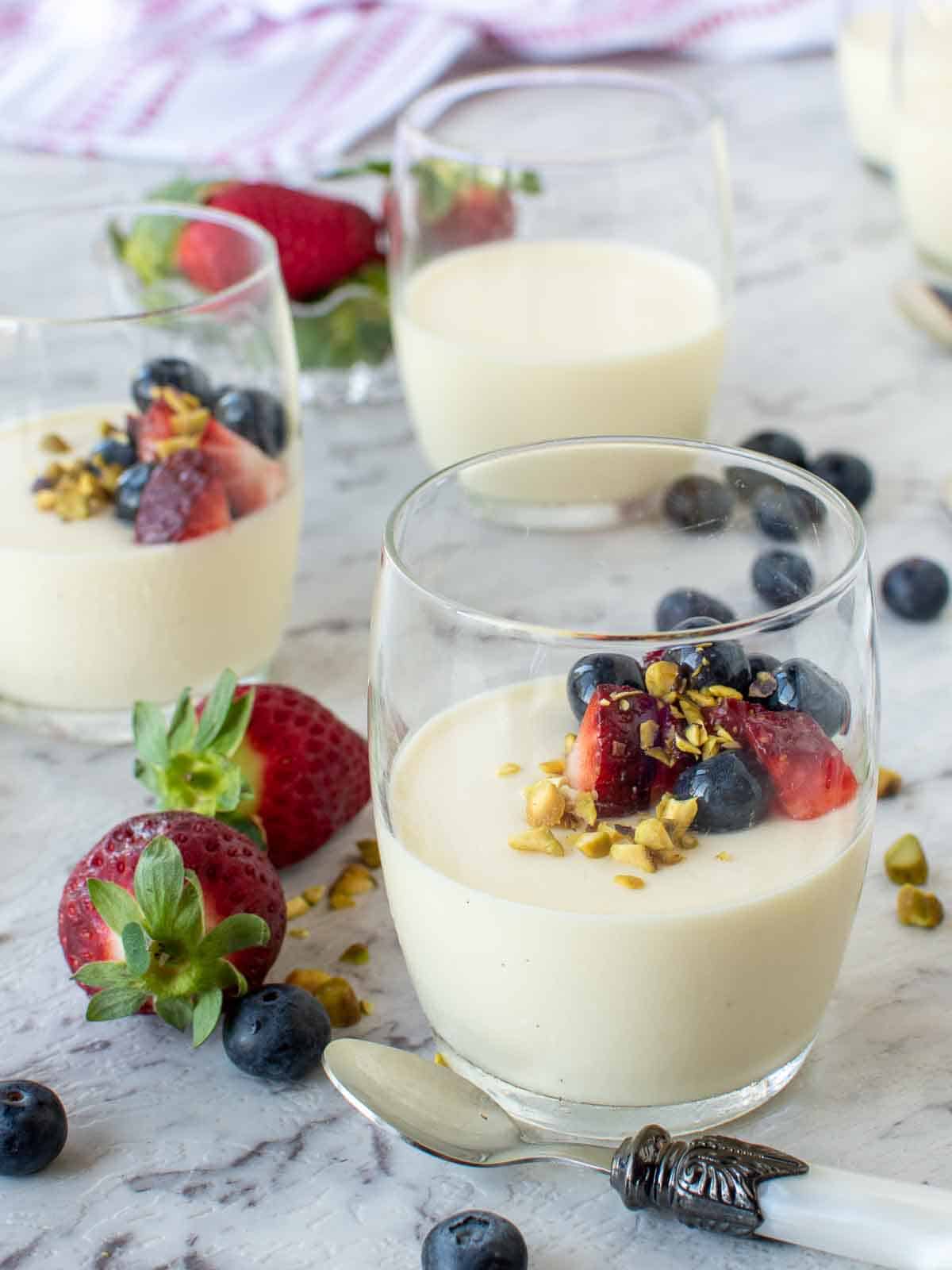 three vanilla panna cotta in glasses with strawberries and blueberries.