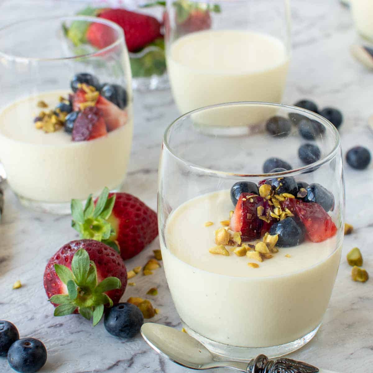 three vanilla panna cotta in glasses with strawberries and blueberries