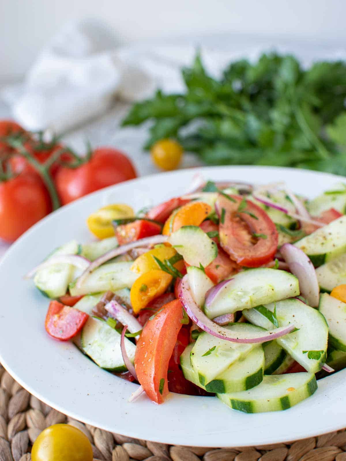 mediterranean cucumber salad on white plate with tomatoes and parsley in the background.