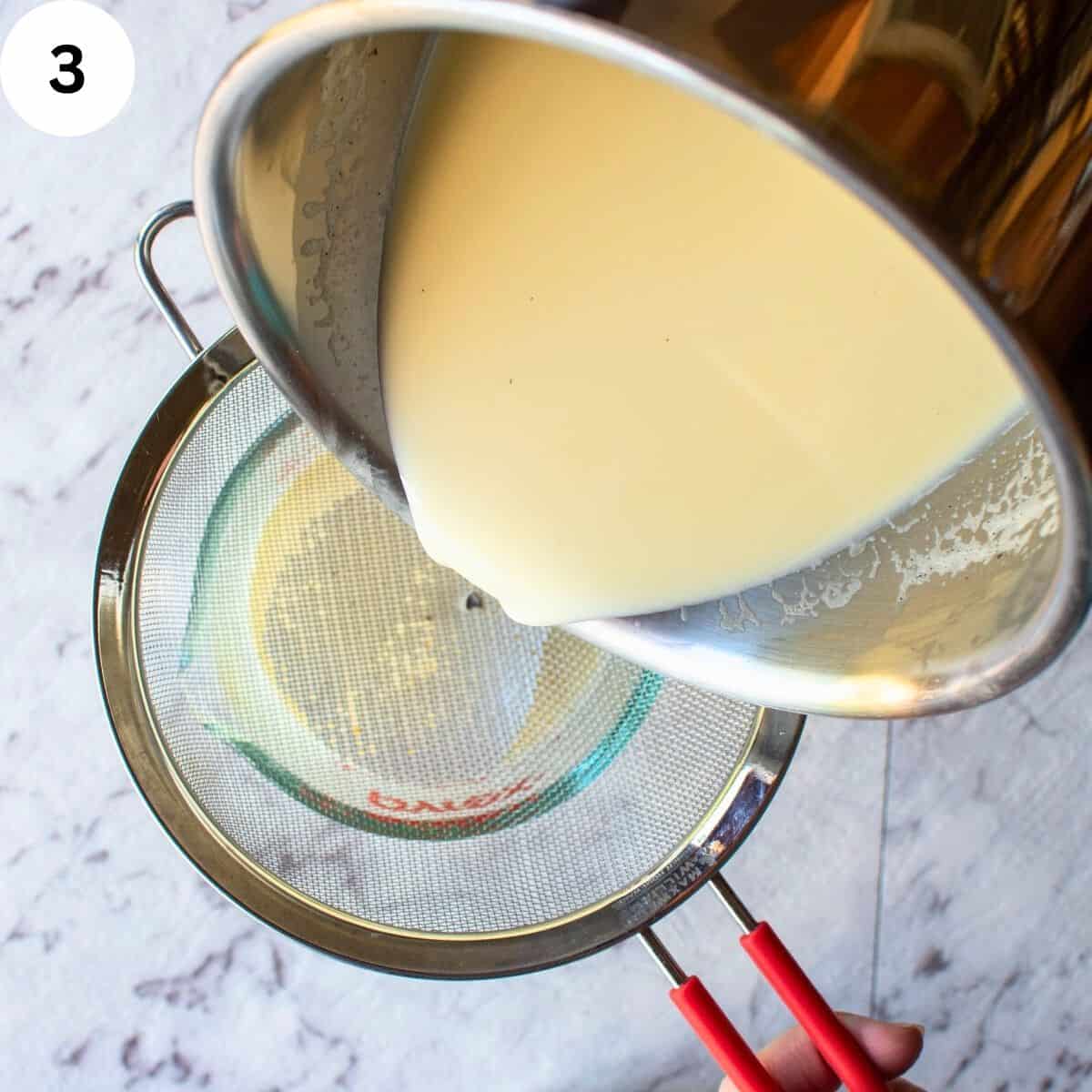 Pouring cream from a saucepan through a sieve into a glass pitcher.