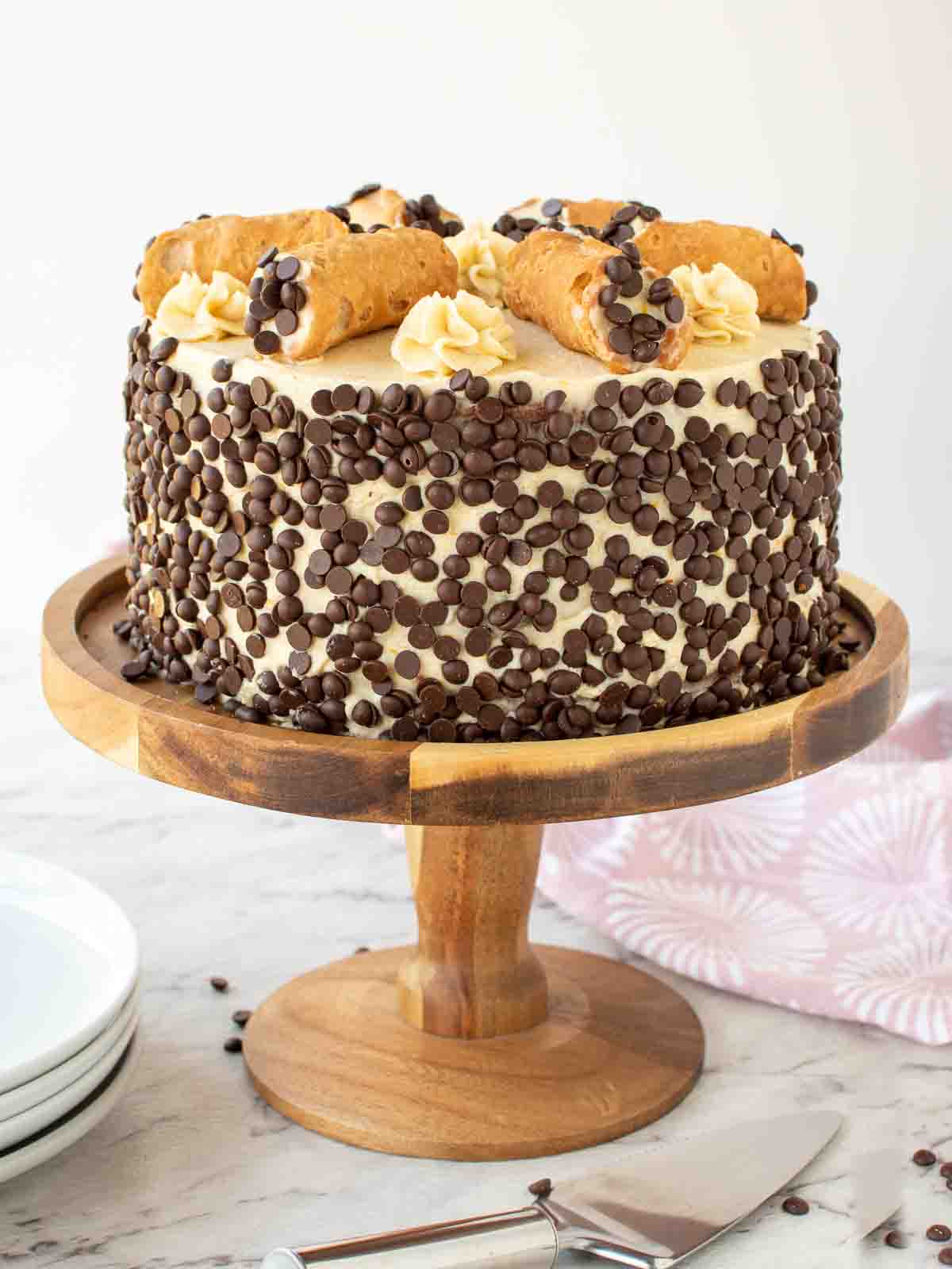 Cannoli Cake covered in mini chocolate chips with six filled cannoli on top.