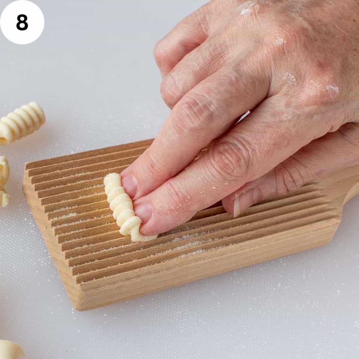 Two fingers using the a ridged board to shape pasta dough.