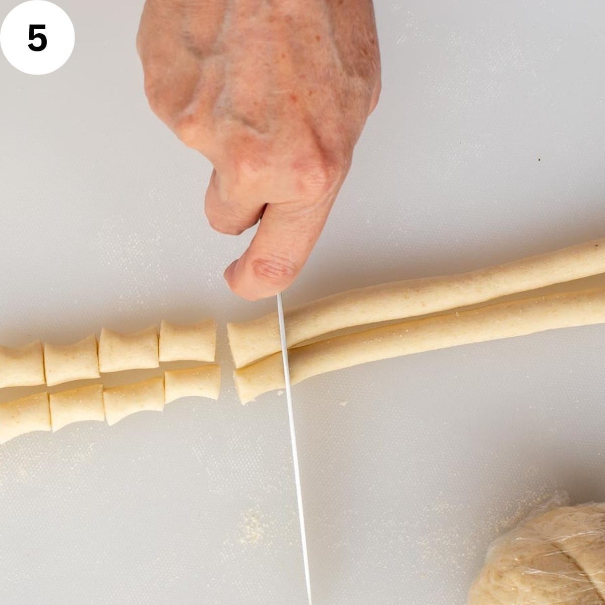 Cutting ropes of semolina pasta into short pieces.