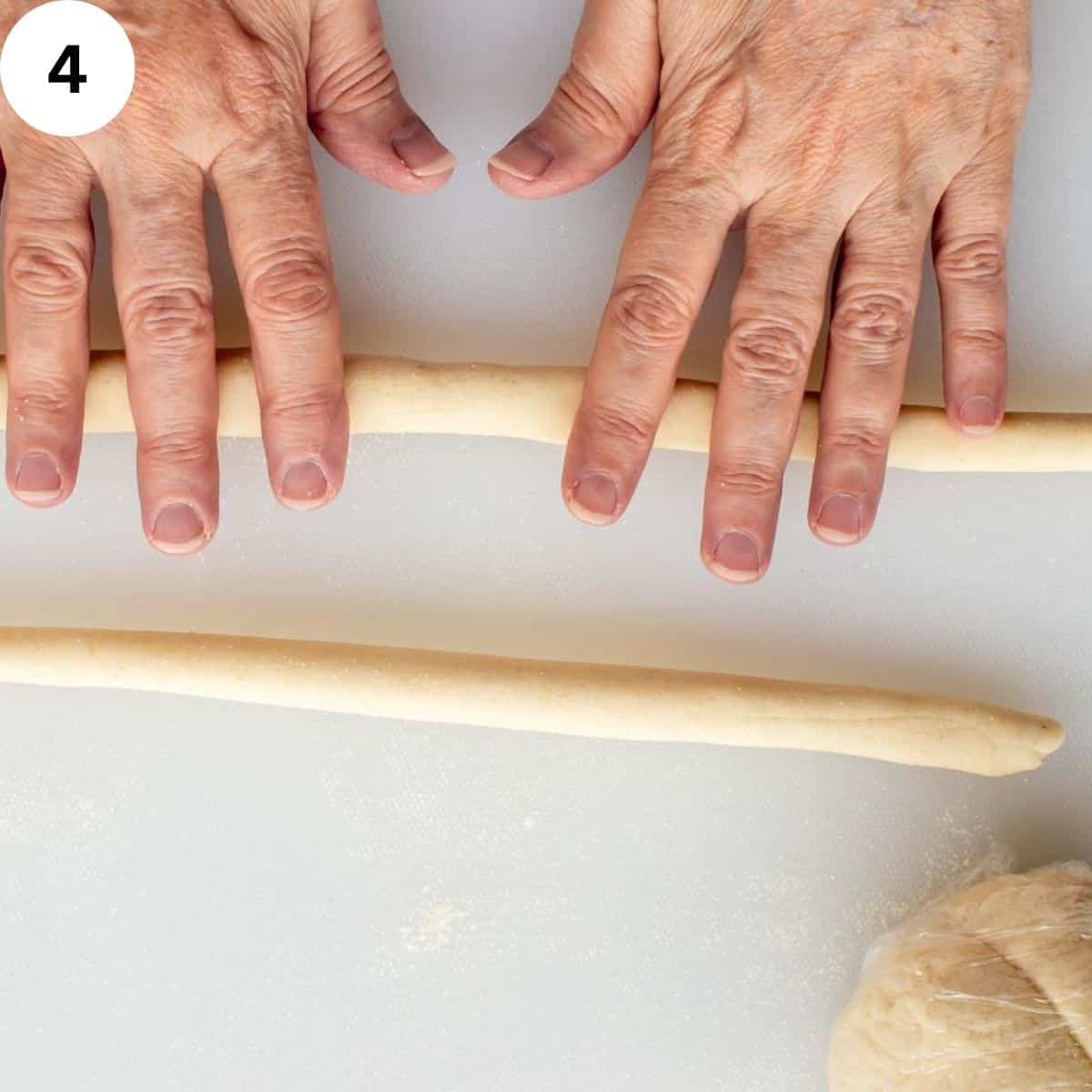 Hands rolling pasta dough into long logs. 
