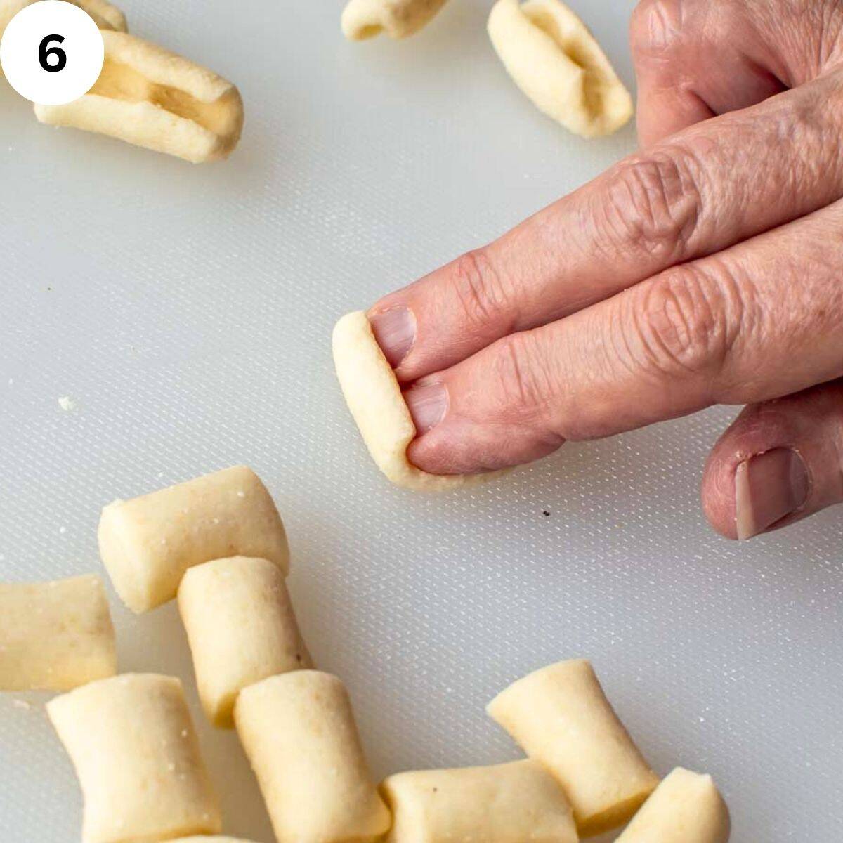 Two fingers rolling short pasta into cavatelli shapes.