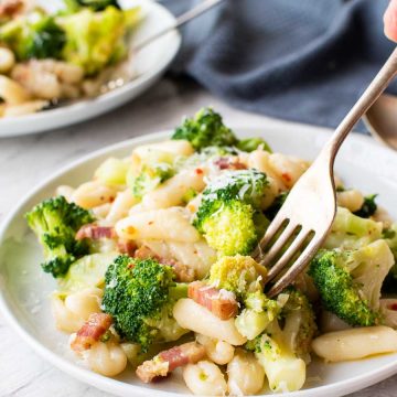 cavatelli and broccoli on white plate and someone taking a forkful of pasta.