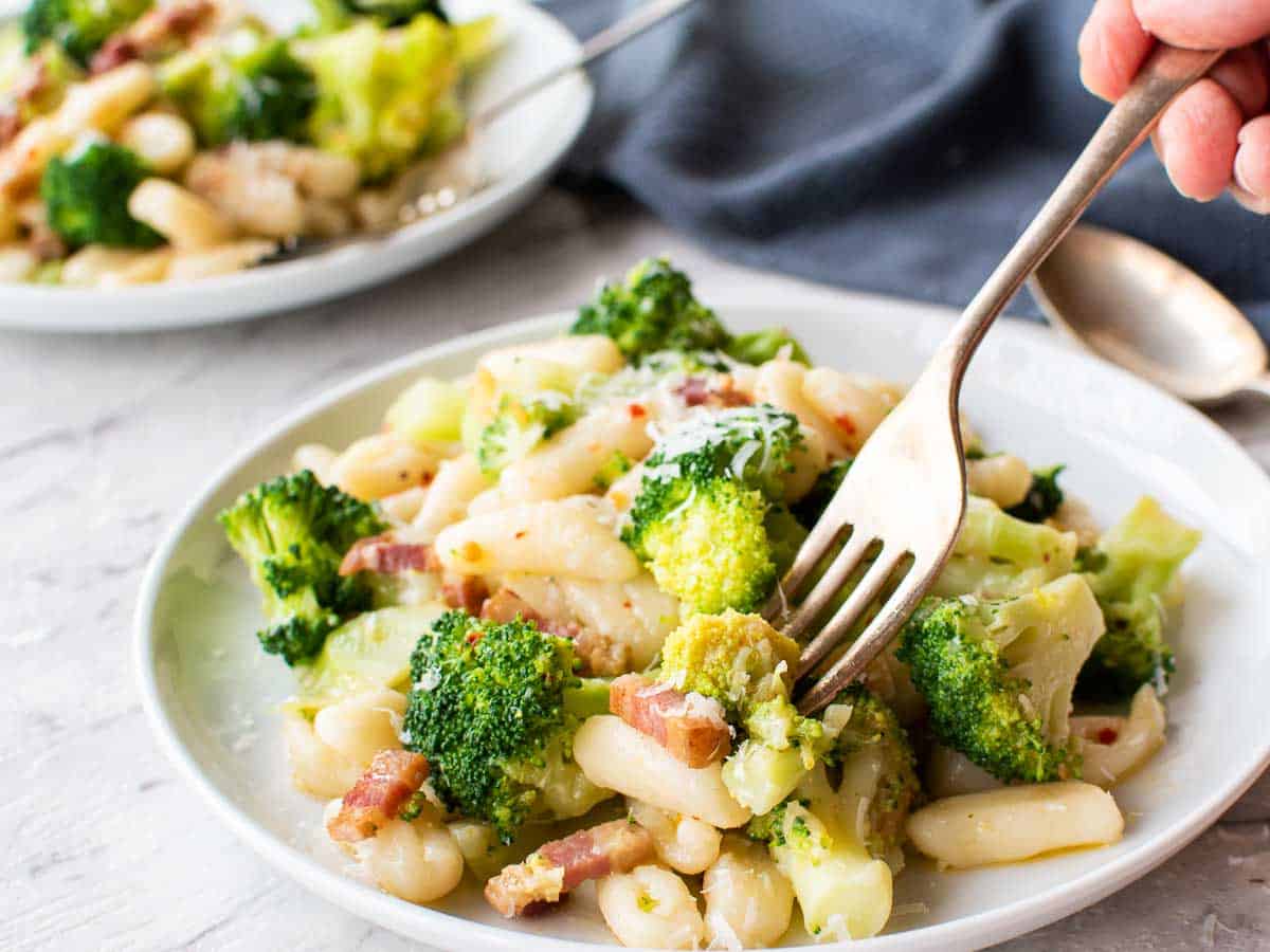 cavatelli and broccoli on white plate and someone taking a forkful of pasta.