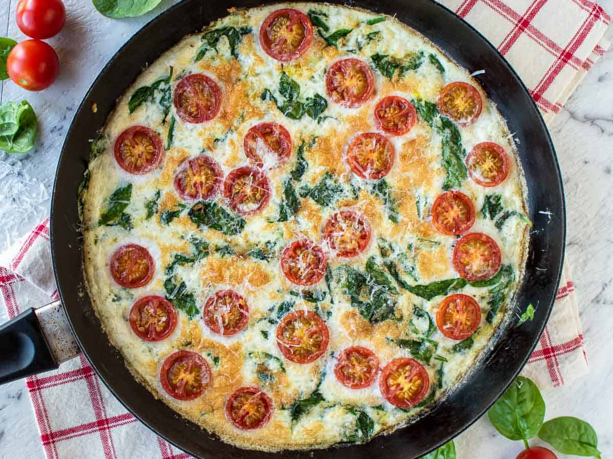 An overhead view of the finished frittata with cherry tomatoes and spinach in black frying pan.