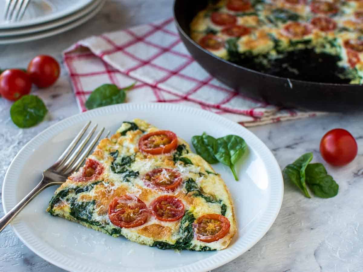 A slice of frittata on a white plate with pan in the background.