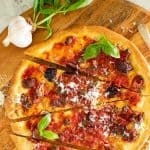 image with text. text reads "homemade calabrese pizza". image is pizza with tomatoes, black olives, anchovies and capers with sprinkling of parmesan cut into four pieces viewed from above.