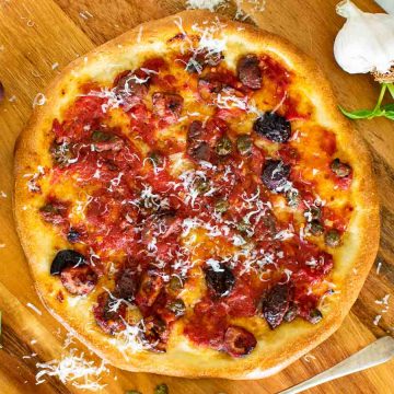 pizza with tomatoes, black olives, anchovies and capers with sprinkling of parmesan viewed from above.