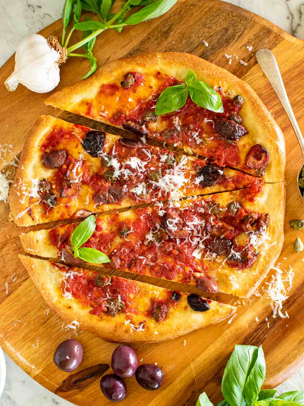 pizza with tomatoes, black olives, anchovies and capers with sprinkling of parmesan cut into four pieces viewed from above.