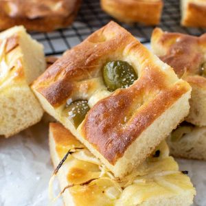 close up of focaccia bread with green olives on top and sliced onions on other pieces