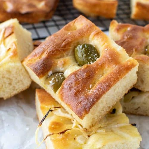 close up of focaccia bread with green olives on top and sliced onions on other pieces