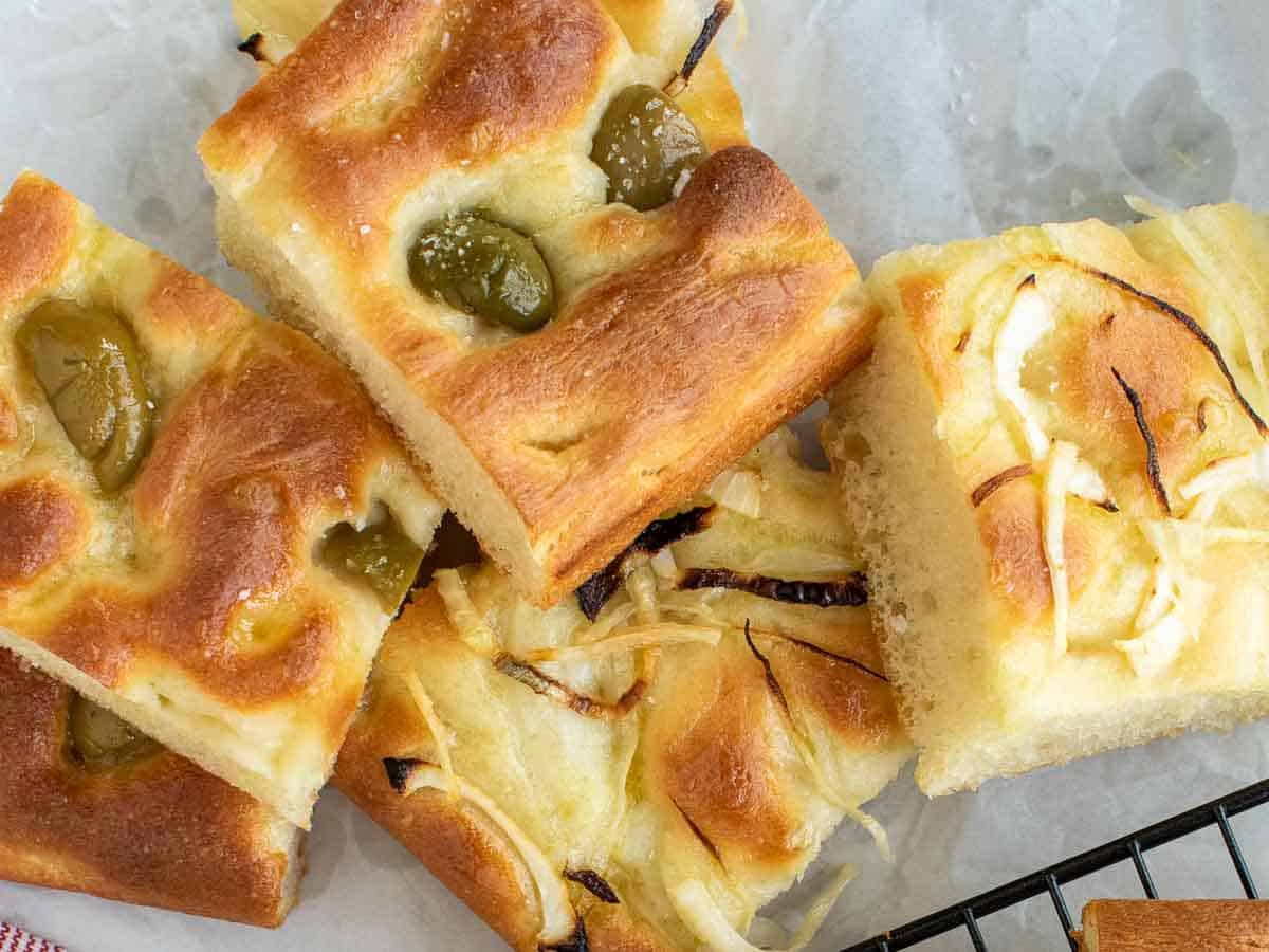 focaccia bread with green olives on top and sliced onions on other pieces viewed from above.