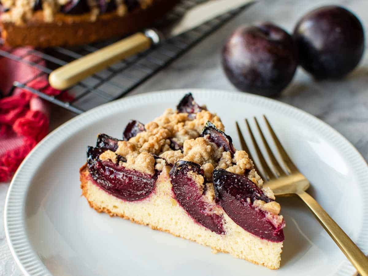 slice of plum cake on white plate with gold fork.