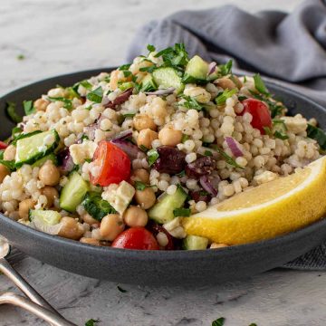 bowl of couscous salad with fork and spoon in the front and grey towel in the background.