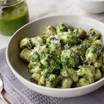 a bowl of pesto gnocchi on a grey cloth with jar of pesto in the background.