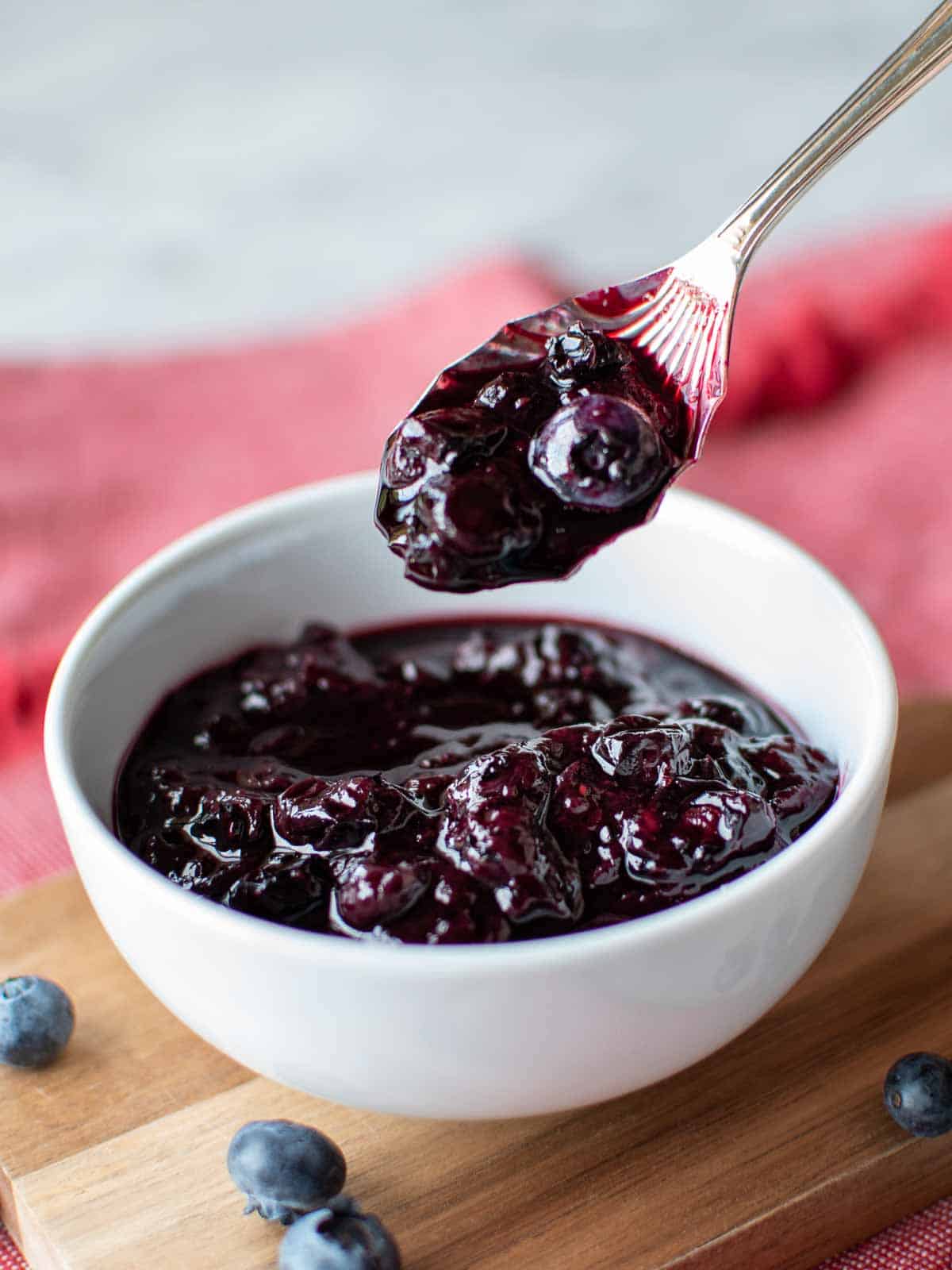 blueberry compote in a white bowl with a spoon full lifted out.