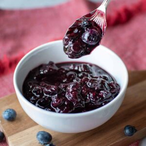 Blueberry compote in a white bowl with a spoonful lifted out.
