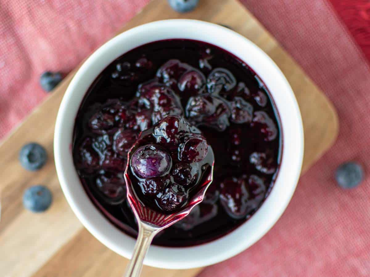 Blueberry sauce in a white bowl with a spoon full lifted out viewed from above.
