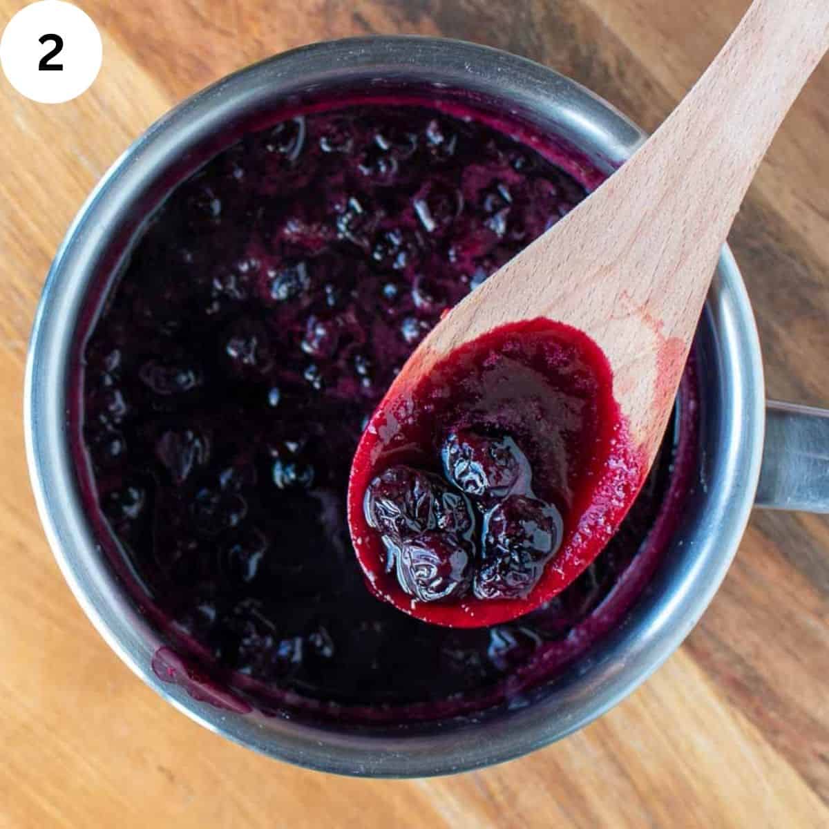Blueberries cooked until soft in a saucepan with wooden spoon.