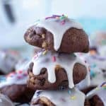 image with text. text reads "the best italian chocolate cookies". image is three chocolate cookies with white frosting and sprinkles stacked with extra cookies around all on a wire rack.