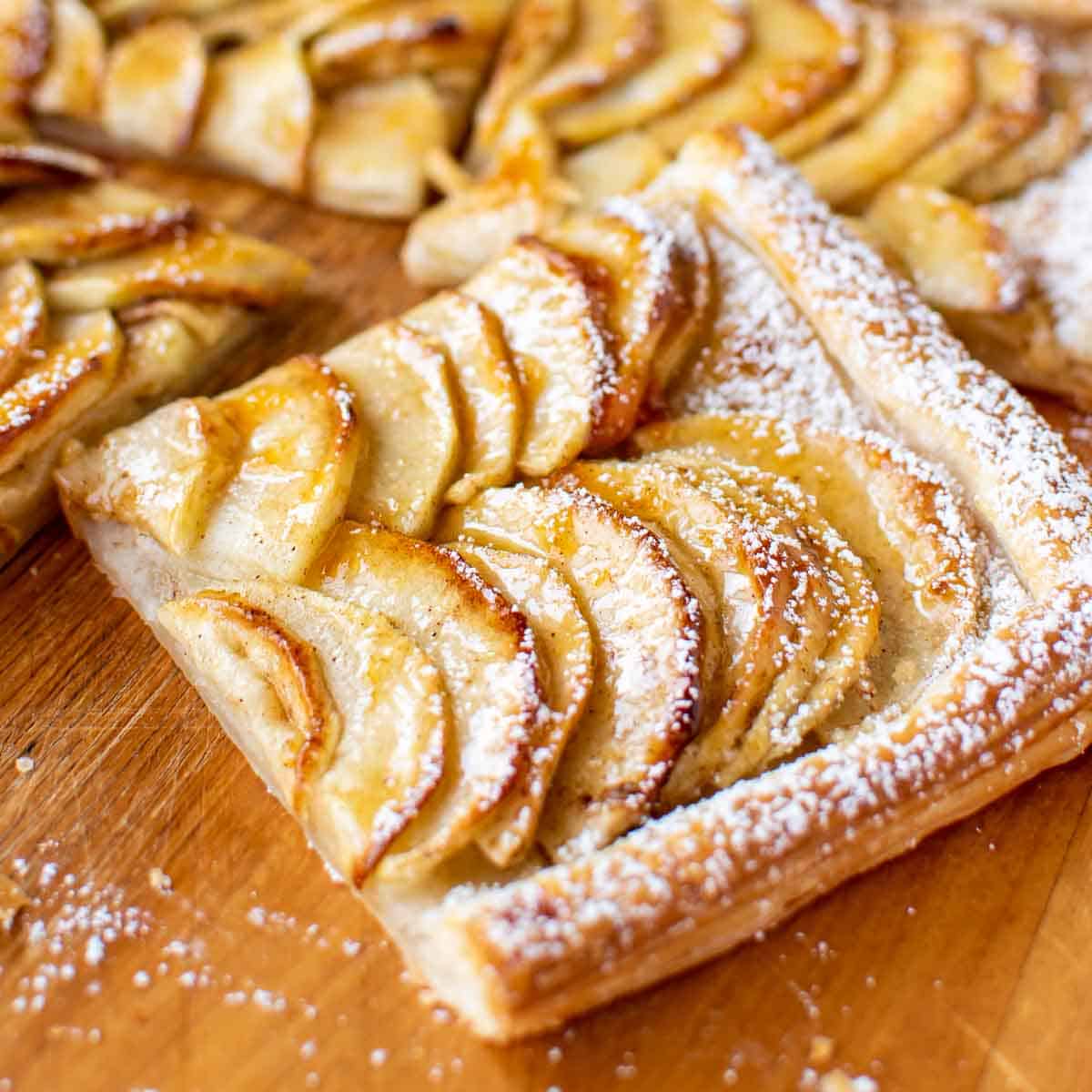 close up slice of puff pastry apple tart on wooden board.