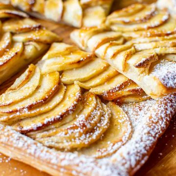 close up slices of puff pastry apple tart on wooden board.