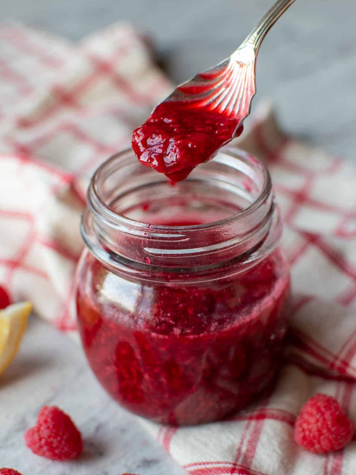 raspberry sauce in a glass jar with a spoon full lifted out.