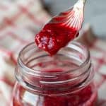 image with text. text reads "only 3 ingredients raspberry compote". image is raspberry compote in a glass jar with a spoon full lifted out.