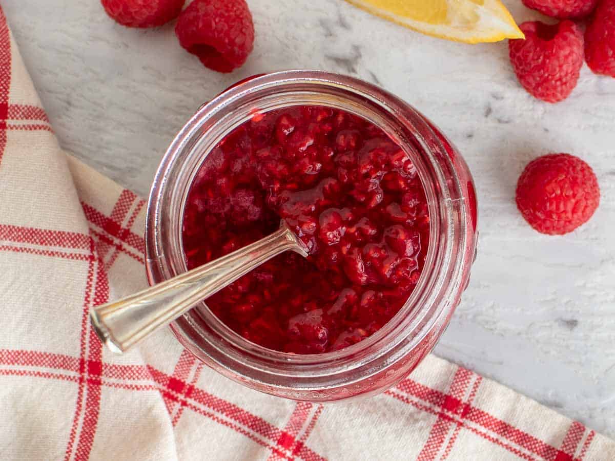 raspberry sauce in a glass jar with spoon insert viewed from above.