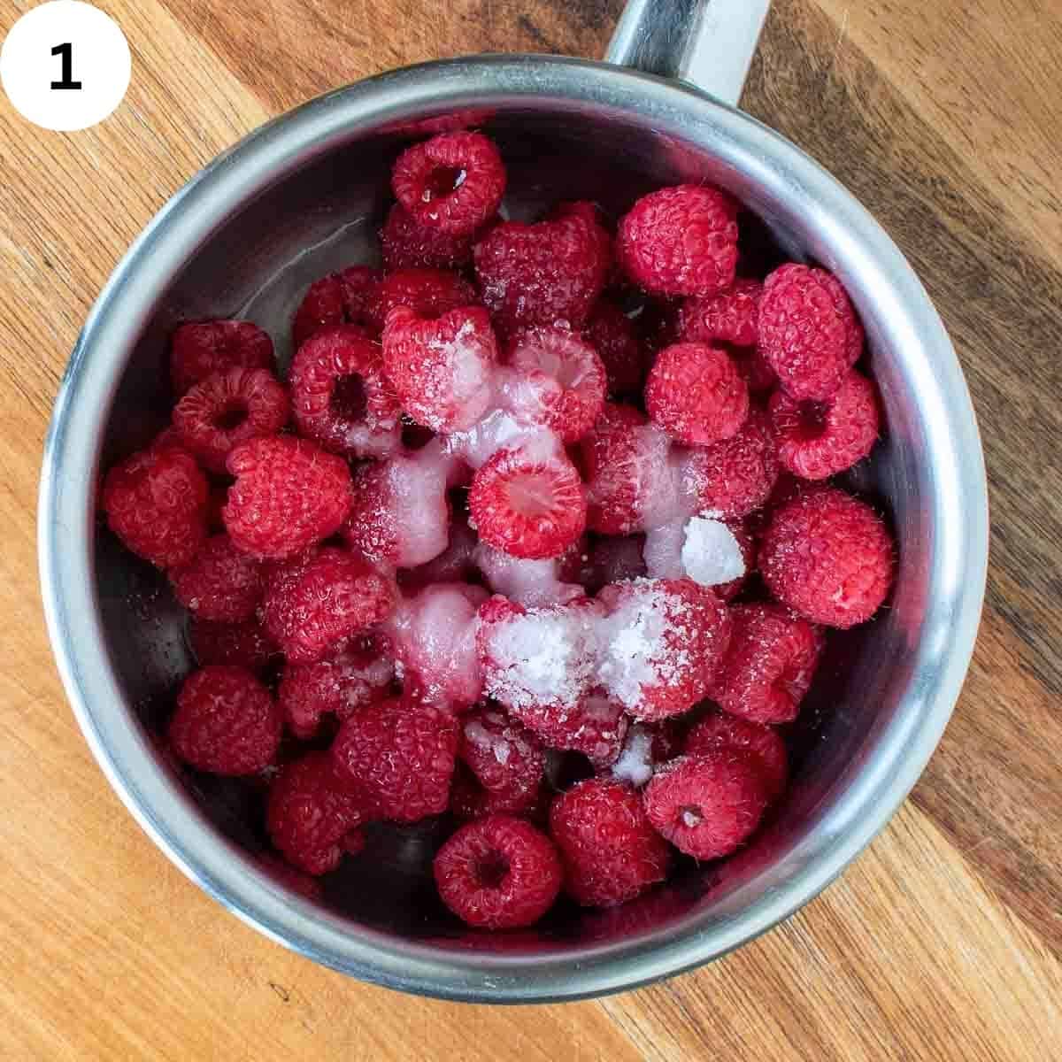 Fresh raspberries and sugar in a stainless steel saucepan.
