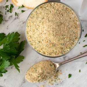 Italian bread crumbs in glass jar with a spoonful of crumbs viewed from above.