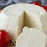 image with text. text reads "how to freeze ricotta cheese". image is whole fresh ricotta cheese on wooden board with a wedge cut out; wedge in front of whole cheese.