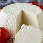 Bild mit Text. der Text lautet "Wie man Ricotta-Käse einfriert". bild ist ganzer frischer Ricotta-Käse auf Holzbrett mit einem Keil ausgeschnitten; Keil vor dem ganzen Käse.