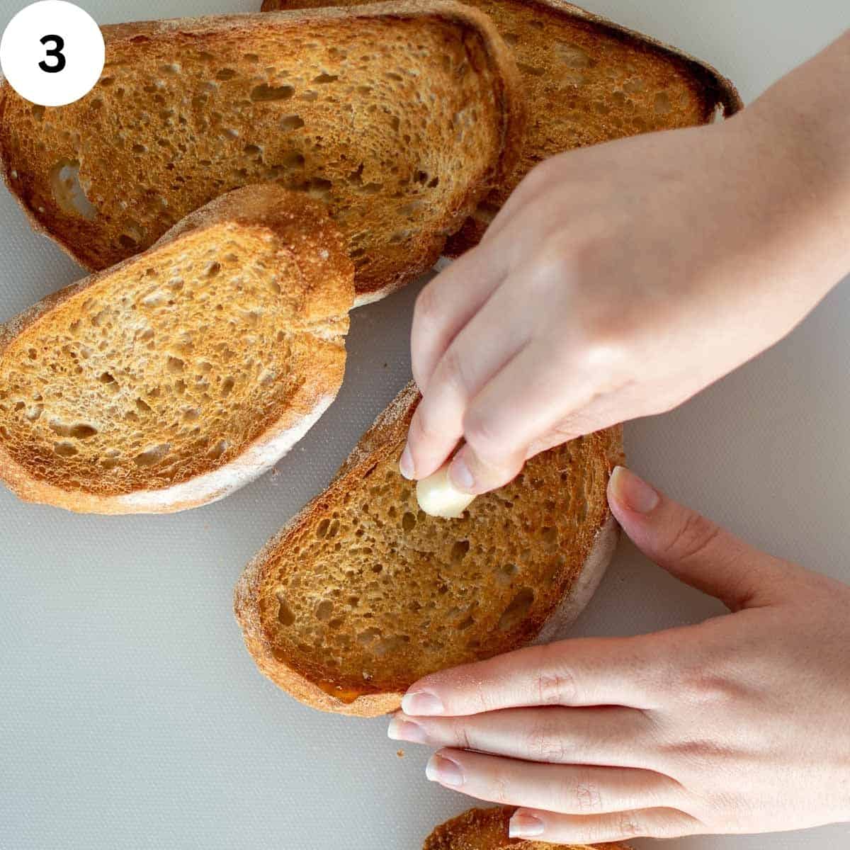 Rubbing garlic over toasted bread slices.