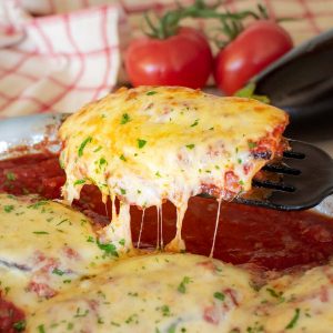 cheese covered chicken cutlet being lifted out of baking dish.